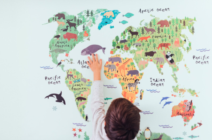 Child pointing at a colorful illustrated world map with animals